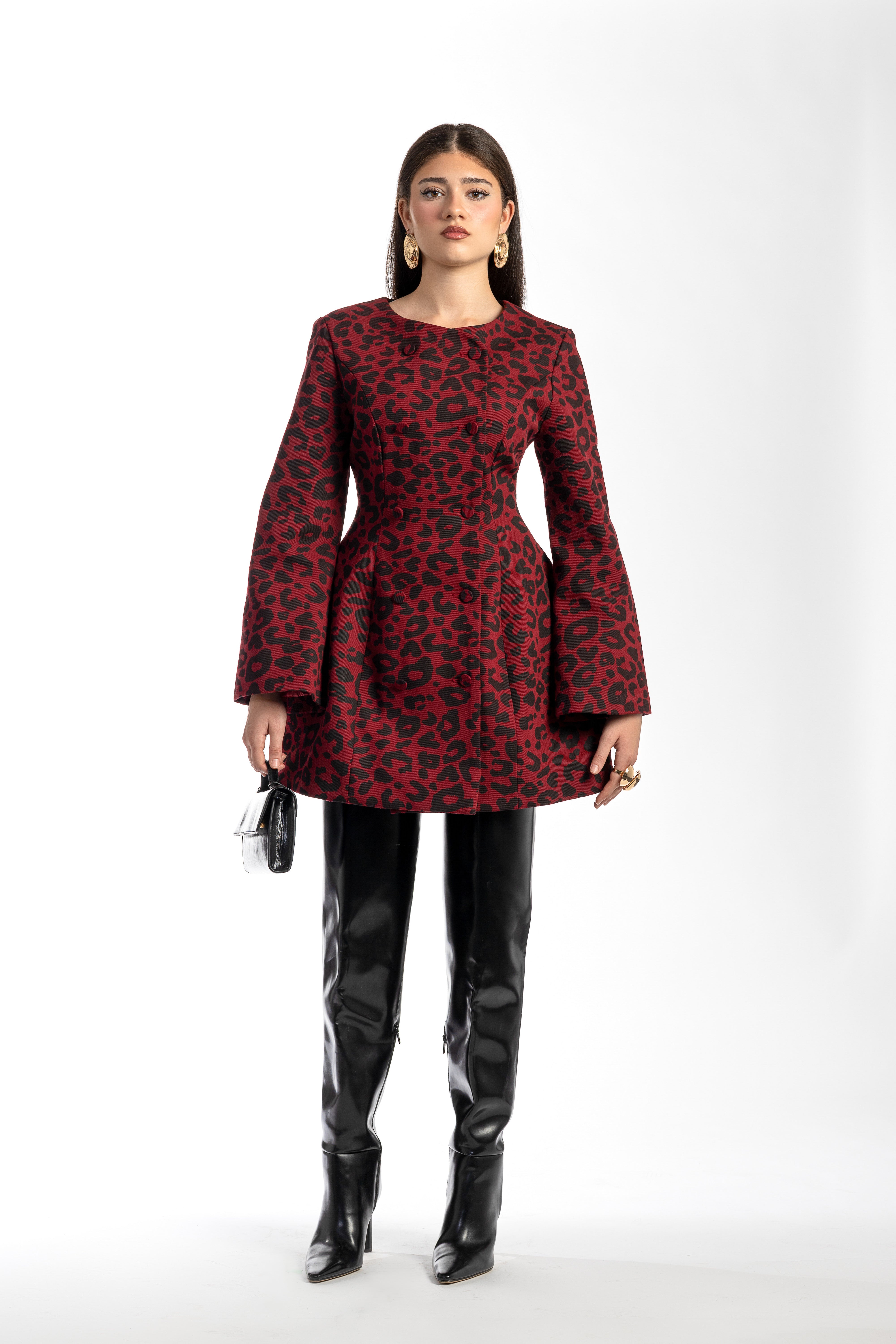 Woman wearing a red leopard print dress with black vinyl leggings and boots on a white background